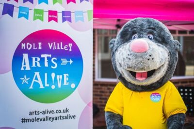 Colour photo of mole mascot next to a colourful Arts Alive banner
